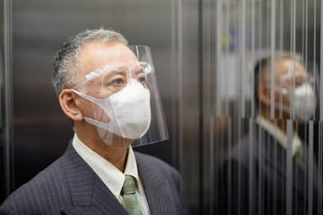 Mature Japanese businessman with mask and face shield thinking inside the elevator