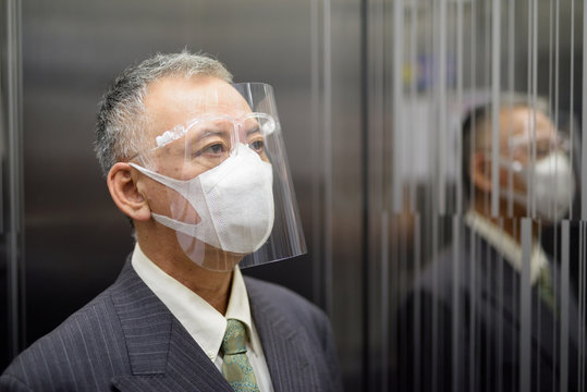 Mature Japanese businessman with mask and face shield thinking inside the elevator