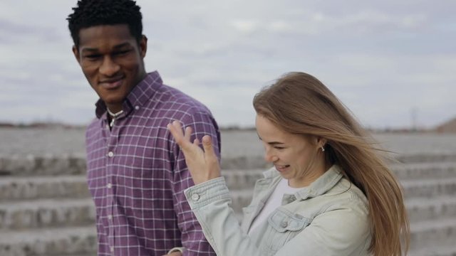 Happy multiracial friends African man and Caucasian woman talks walking in a city embankment