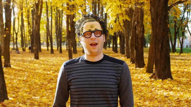 A young guy in a wacky mask on his face rejoices in autumn and looks at the camera, emotion
