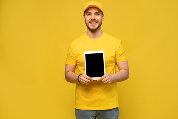 Cool delivery man with tablet. demonstrates tablet. looking at camera. isolated on yellow background.