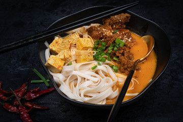 Vegan Thai rec curry with noodles, tofu and seitan served in black bowl