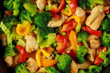 Healthy stir fry vegetables with chicken in pan on white surface. Close up.