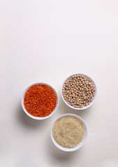 Rice, lentils, chickpeas in white bowls on a light yellow background. Healthy food concept. Top view.