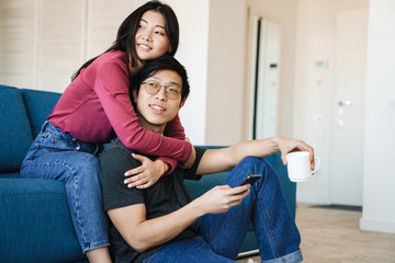 Photo of asian couple holding cup and mobile phone while sitting