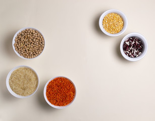 Rice, lentils, chickpeas, peas, beans in white bowls on a light yellow background. Vegan food concept. Horizontal orientation. Top view. Copy space.