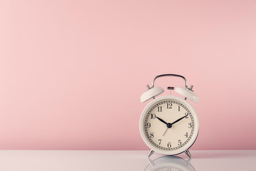  белый будильник на белом столе и розовом фоне