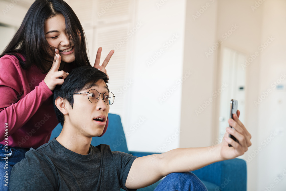 Sticker Photo of asian couple making horns and taking selfie on cellphone