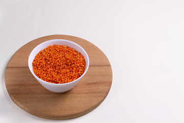 Orange lentils in a white bowl on a round cutting board. Healthy food concept. Copy space.