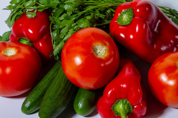 Vegetables tomatoes, cucumbers, bell peppers and parsley close-up on a light background.