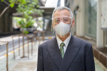 Mature Japanese businessman with mask and face shield in the city