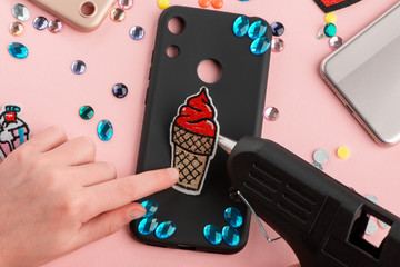 Girl attaching embroidered patches and rhinestones onto black phone case