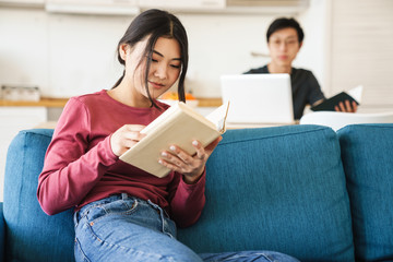 Photo of young concentrated asian couple reading books and using laptop