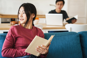 Naklejka premium Photo of young concentrated asian couple reading books and using laptop