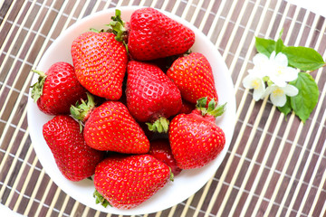 ripe strawberries on a white plate and jasmine flowers