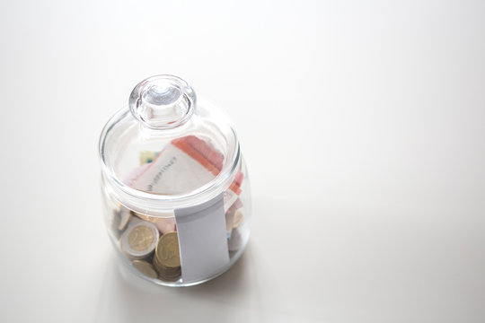 Jar of glass with metal coins and paprer money on white table save for future