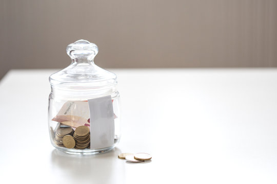Jar of glass with metal coins and paprer money on white table save for future