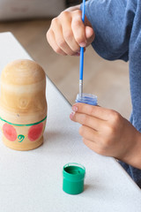 A child paints a wooden blank of a nesting doll. Children's crafts