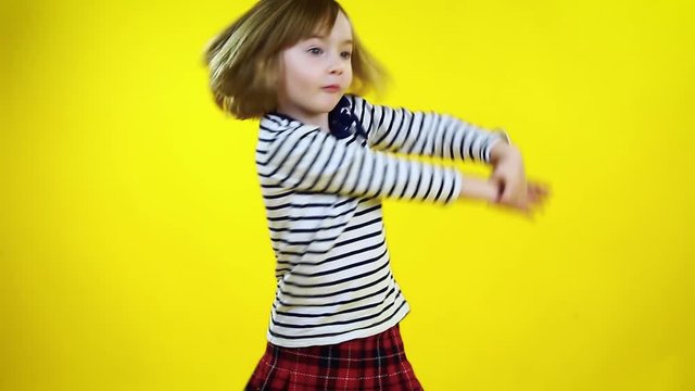 Happy little girl in red hat dancing over yellow background. Cute blonde child.