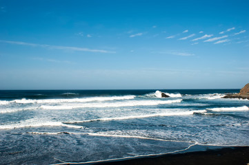 Blue sky, azure sea, waves breaking on the rocky shore. Meeting of the sky, sea and earth. Raging blue sea. Playa de Benijo, Spain.