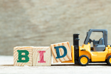 Toy forklift hold letter block d to complete word bid on wood background