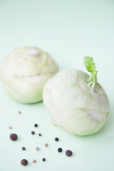 Two kohlrabies with some peppercorns and allspice on a paper background. Light mint green background. 