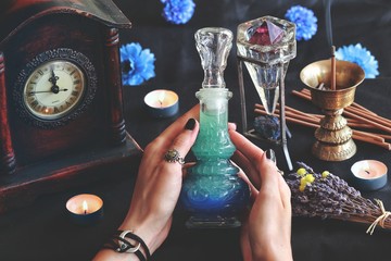 Wiccan witch holding lucid dreaming good night potion in her hands at her altar. Blue colored...