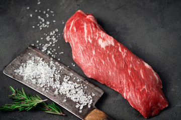Raw tenderloin of beef or skirt steak with a hatchet for meat, salt and rosemary on a dark stone...