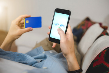 Close up man hand lying on the sofa doing shopping online with smartphone holding credit card for internet payment. Home banking and technology concept. 