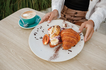 Closeup of female hands having coffee with croissants in outdoor terrace at cafe. Girl holds a coffee mug. on the background of a croissant. coffee with a croissant. Beginning of the morning