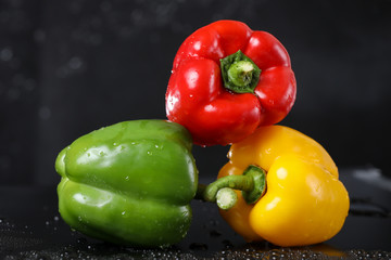 Horizontal view of red, green and yellow sweet paprika under the water drops in a black background. Healthy lifestyle.