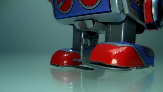 An antique cheerful colorful metal clockwork robot goes, on a light background. Legs of a robot walking on a glass surface. Macro. Closeup. Shallow depth of field  