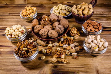 Various nuts (almond, cashew, hazelnut, pistachio, walnut) in bowls on a wooden table. Vegetarian meal. Healthy eating concept