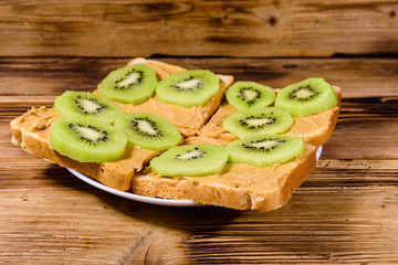 Sandwiches with peanut butter and sliced kiwi fruits in plate on a wooden table