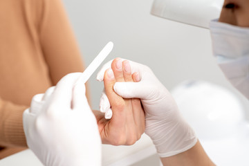 Close up of hands of manicure master doing manicure procedure by nail file.