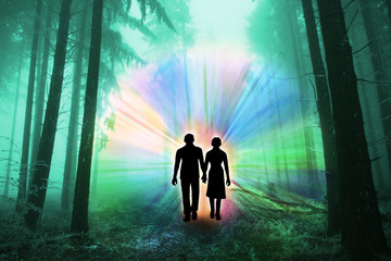 black silhouettes of man and woman with luminous rays of energy in a dark forest on the road among the trees, the concept of aura, living energy, death and the transition to another world