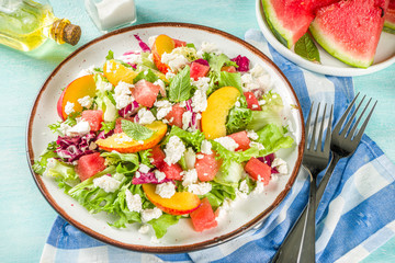 Summer diet salad with leaves of lettuce, watermelon, peach and feta cheese. On a light blue background copy space
