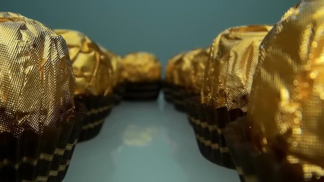The camera moves slowly next to rows of tasty and beautiful chocolate balls bonbon with golden wrapper . Macro. Closeup. Shallow depth of field. Ultra small special camera