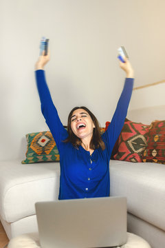 Vertical image. Exited young woman on computer holding credit cards raising arms. Happy for new purchase or more money. Online shopping, home banking, technology, easy payment or savings concept.