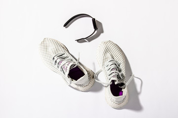 White running shoes, a sports watch on a white background under the natural light of the morning sun. Concept of jogging, running, hard workout. Banner. Flat lay, top view
