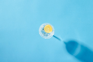 A glass of refreshing water with ice and lemon on a blue background. Heat concept, fresh. Natural light. Flat lay, top view