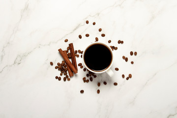 Cup with coffee, coffee beans and cinnamon sticks on a marble background. Flat lay, top view