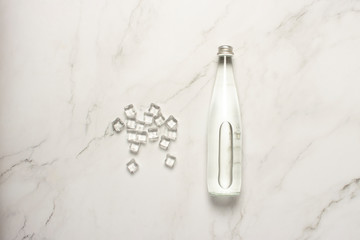 Glass bottle of water and ice cubes on a marble table. The concept of heat, water balance, diet, weight loss, refreshing drinks. Flat lay, top view