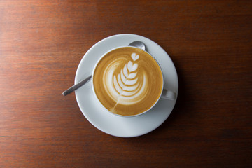 Top-view shot of single cup of latte coffee with art cream foam in white ceramic cup on wooden...