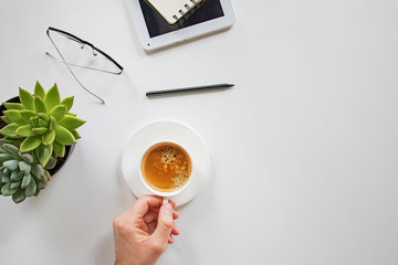 Man's hand holding cup of coffee on his workplace