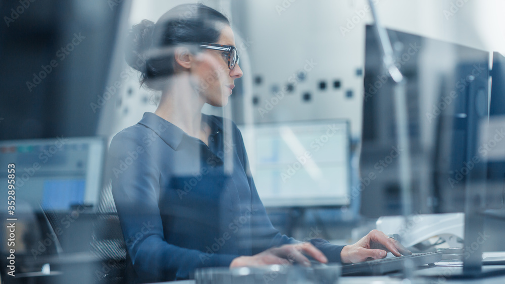 Poster shot through glass. female engineer working on personal computer. she is working in office in modern