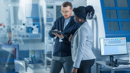Female Industrial Engineer stands with Male Project Supervisor, They Use Tablet Computer and Discuss Modern Factory Planning. Manufacturing Facility with CNC Machinery and Robot Arm Assembly Line © Gorodenkoff