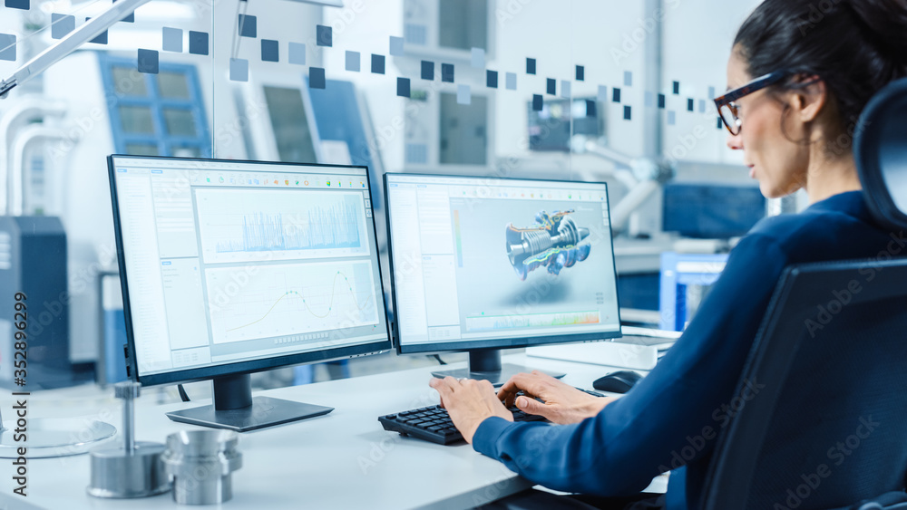 Fototapete Industrial Female Engineer Working on a Personal Computer, Two Monitor Screens Show CAD Software with 3D Prototype of New Hybrid Hydrogen Engine and Charts. Modern Factory with High-Tech Machinery