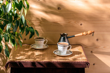 Two cups of coffee and cezve on the table in the patio lit by morning sun.