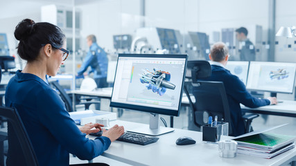 Industrial female Engineer Working on a Personal Computer, Screen Shows CAD Software with 3D Prototype of Electric Engine. In Background Modern Factory with High-Tech CNC Machinery - obrazy, fototapety, plakaty